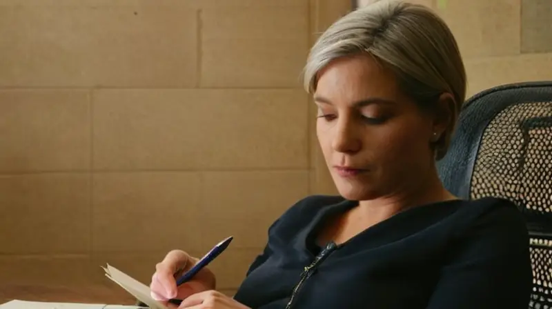 Una estudiante se prepara para un examen escribiendo notas y corrigiendo errores en su libreta, con una concentración intensa en sus ojos