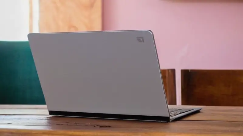 Una laptop moderna se encuentra en una mesa vieja de madera, cubierta en parte por un carpeta gris plana